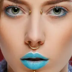 Dziewczyna z zielonymi oczami, błękitnymi ustami i złotymi kolczykami: septum, bridge piercing i w uchu.