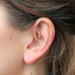 Złoty kolczyk w uchu, ozdobiony cyrkoniami, stanowi subtelny akcent. Ten rook piercing dodaje elegancji.