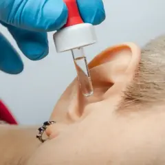 Krople do ucha z pipetki, gdy ropieje ucho od kolczyka. Ręka w niebieskiej rękawiczce aplikuje płyn.