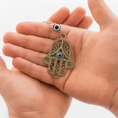 Dłonie trzymają ozdobny amulet ręka Fatimy z niebieskim okiem, symbol ochrony.