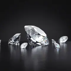 Kilka brylantów, w tym jeden duży, błyszczy na ciemnym tle. Każdy diament jest oszlifowany, by maksymalnie odbijać światło.