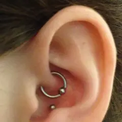 Kolczyk w uchu, ozdoba typu kółko z kulką w miejscu anti tragus, obok mniejsza kuleczka.
