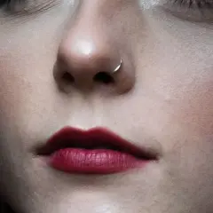 Delikatny kolczyk w nosie, niczym mantis piercing, podkreśla usta w odcieniu głębokiej czerwieni.