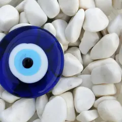 Niebieskie oko proroka znaczenie - amulet chroniący przed złym spojrzeniem, leżący na białych kamieniach.