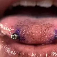 Język z dwoma kolczykami, przypominającymi snake eye piercing. Widać fioletowy ślad po markerze.