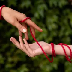 Dwie dłonie połączone czerwoną nitką symbolizują przeznaczenie. Co oznacza czerwona nitka na nadgarstku? To więź, która nigdy nie zostanie zerwana.
