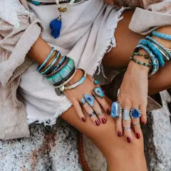 Kobieta w boho stylu nosi liczne bransolety i pierścionki z kamieniami, w tym amazonit, który symbolizuje spokój i harmonię.