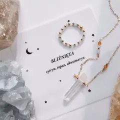 Biżuteria z kamieni dla Bliźniąt: naszyjnik z kryształem i pierścionek na tle surowych minerałów.