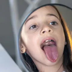 Dziewczynka w lustrze pokazuje swój język, który wygląda jak mały, różowy **tongue web**.