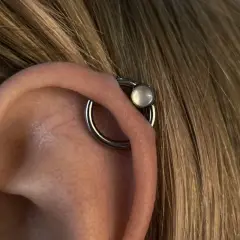 Obrączka z białym kamieniem, czyli orbital piercing, zdobi ucho.