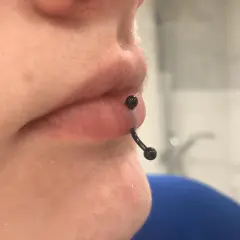 Zbliżenie na usta z czarnym kolczykiem typu vertical labret, który przechodzi pionowo przez dolną wargę.