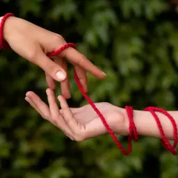 Dwie dłonie połączone czerwoną nitką symbolizują przeznaczenie. Co oznacza czerwona nitka na nadgarstku? To więź, która nigdy nie zostanie zerwana.