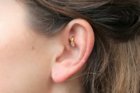 Złoty kolczyk w uchu, ozdobiony cyrkoniami, stanowi subtelny akcent. Ten rook piercing dodaje elegancji.