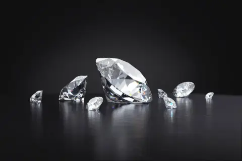 Kilka brylantów, w tym jeden duży, błyszczy na ciemnym tle. Każdy diament jest oszlifowany, by maksymalnie odbijać światło.