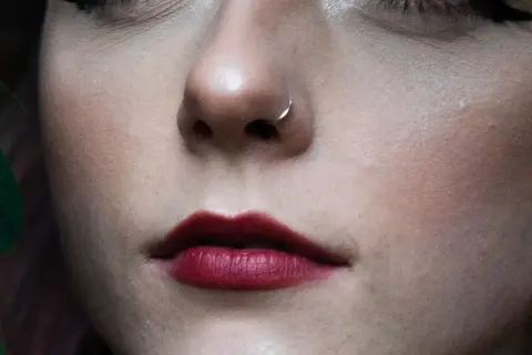 Delikatny kolczyk w nosie, niczym mantis piercing, podkreśla usta w odcieniu głębokiej czerwieni.