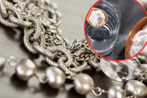 Srebrny naszyjnik i perły czekają na czyszczenie biżuterii. W szklance woda, na łyżeczce soda oczyszczona – domowy sposób na blask.