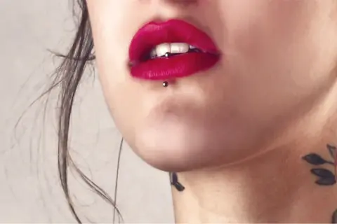Usta z czerwoną szminką i ashley piercing. Delikatny tatuaż na szyi dodaje uroku.