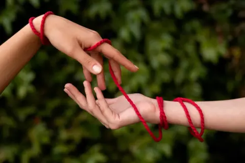 Dwie dłonie połączone czerwoną nitką symbolizują przeznaczenie. Co oznacza czerwona nitka na nadgarstku? To więź, która nigdy nie zostanie zerwana.