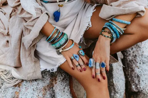 Kobieta w boho stylu nosi liczne bransolety i pierścionki z kamieniami, w tym amazonit, który symbolizuje spokój i harmonię.