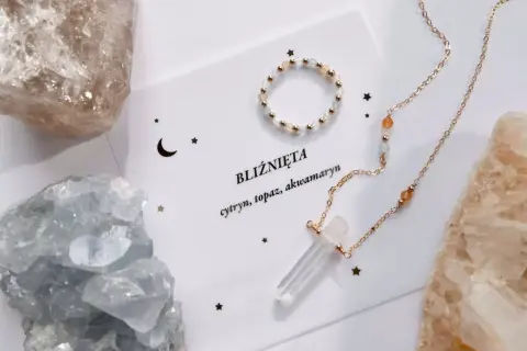 Biżuteria z kamieni dla Bliźniąt: naszyjnik z kryształem i pierścionek na tle surowych minerałów.