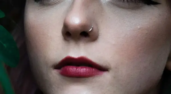 Delikatny kolczyk w nosie, niczym mantis piercing, podkreśla usta w odcieniu głębokiej czerwieni.