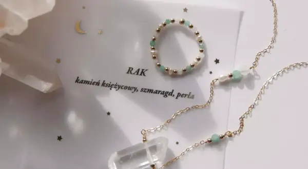 Złota biżuteria z kryształem górskim, perłami i zielonymi kamieniami na karcie z napisem "Rak".
