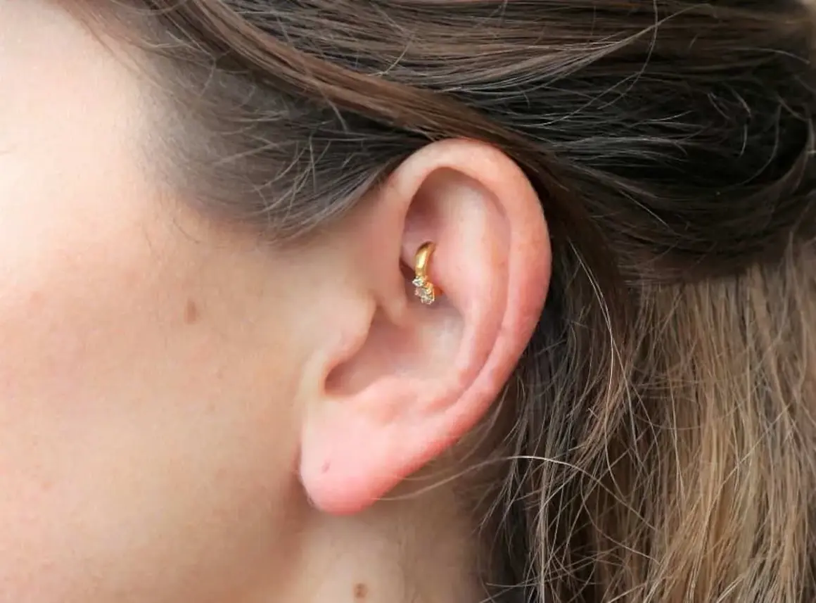 Złoty kolczyk w uchu, ozdobiony cyrkoniami, stanowi subtelny akcent. Ten rook piercing dodaje elegancji.