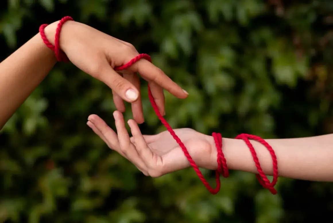 Dwie dłonie połączone czerwoną nitką symbolizują przeznaczenie. Co oznacza czerwona nitka na nadgarstku? To więź, która nigdy nie zostanie zerwana.