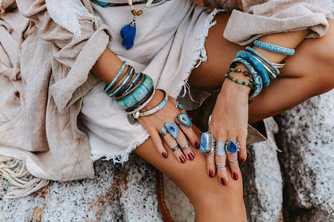 Kobieta w boho stylu nosi liczne bransolety i pierścionki z kamieniami, w tym amazonit, który symbolizuje spokój i harmonię.