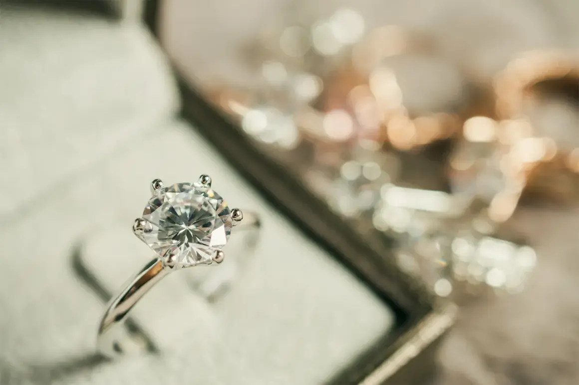 Pierścionek z brylantem w pudełku, otoczony innymi błyszczącymi ozdobami. Ten piękny metal szlachetny lśni w świetle.