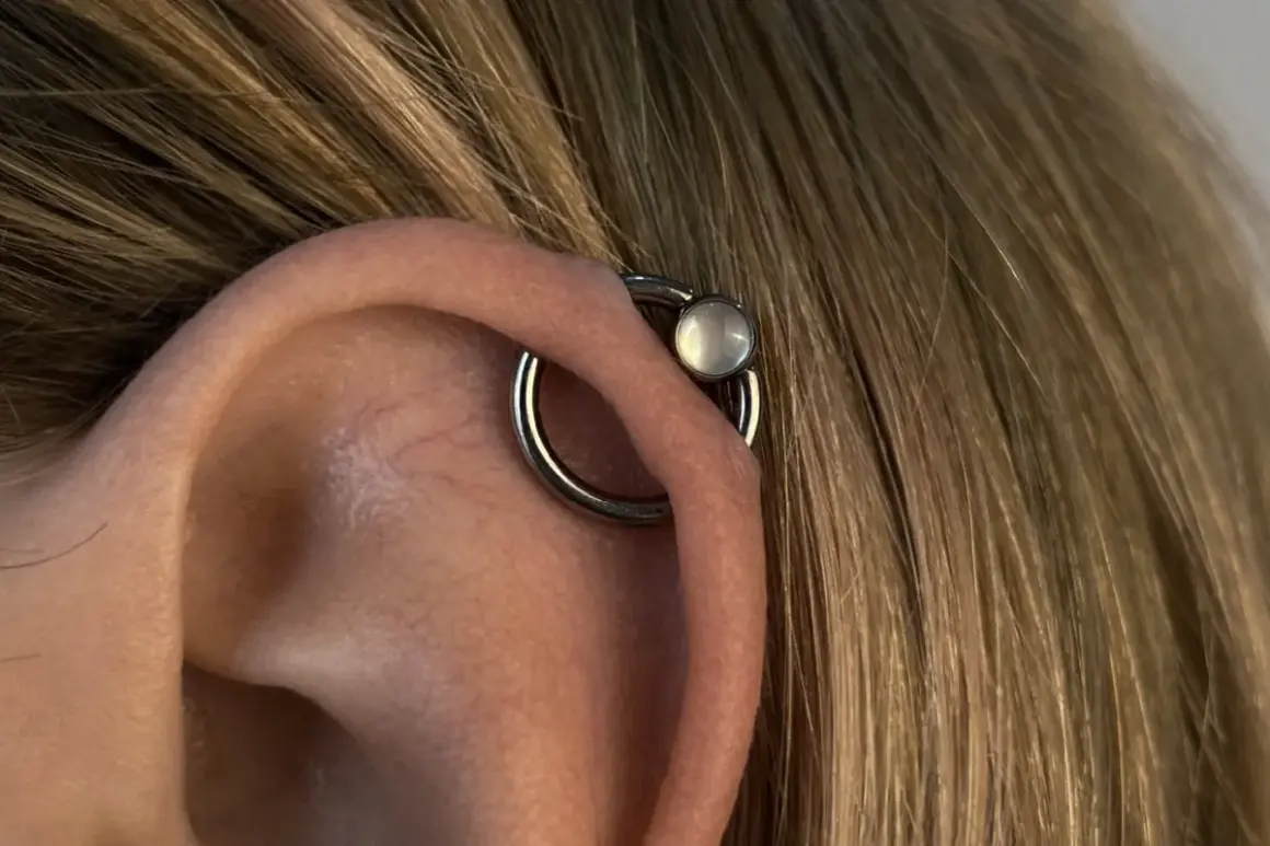 Obrączka z białym kamieniem, czyli orbital piercing, zdobi ucho.