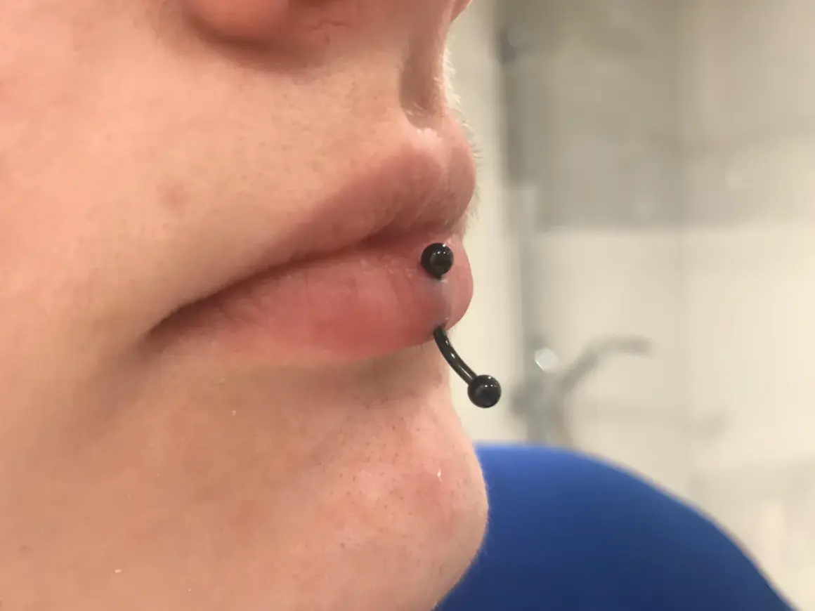 Zbliżenie na usta z czarnym kolczykiem typu vertical labret, który przechodzi pionowo przez dolną wargę.