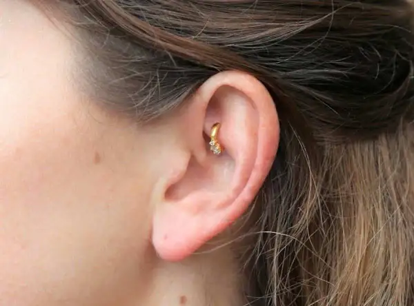 Złoty kolczyk w uchu, ozdobiony cyrkoniami, stanowi subtelny akcent. Ten rook piercing dodaje elegancji.