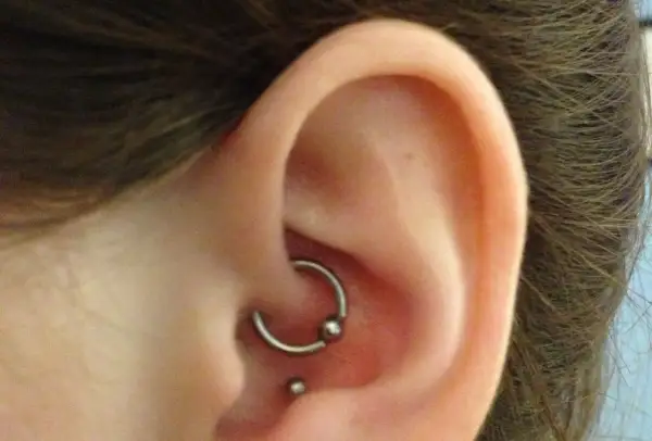 Kolczyk w uchu, ozdoba typu kółko z kulką w miejscu anti tragus, obok mniejsza kuleczka.