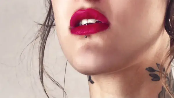 Usta z czerwoną szminką i ashley piercing. Delikatny tatuaż na szyi dodaje uroku.