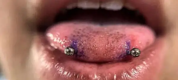Język z dwoma kolczykami, przypominającymi snake eye piercing. Widać fioletowy ślad po markerze.