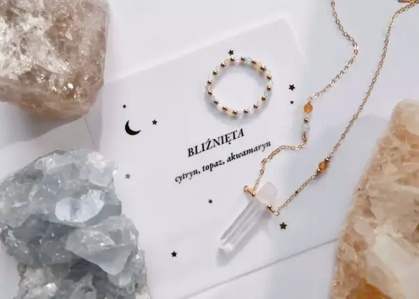 Biżuteria z kamieni dla Bliźniąt: naszyjnik z kryształem i pierścionek na tle surowych minerałów.