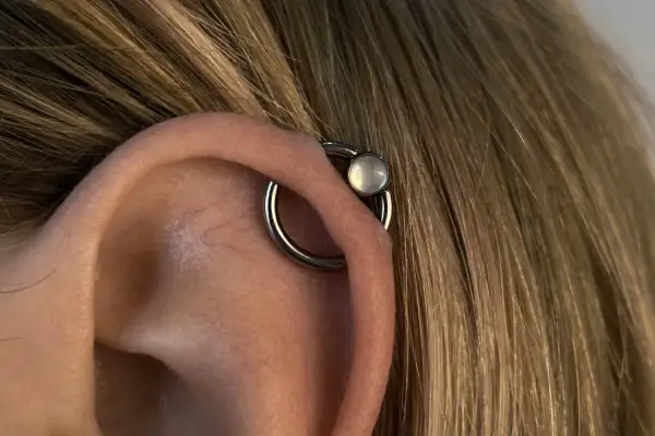 Obrączka z białym kamieniem, czyli orbital piercing, zdobi ucho.