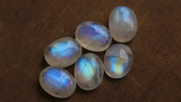 Sześć gładkich, owalnych kamieni księżycowych z niebiesko-żółtym połyskiem, ułożonych na drewnianym tle.